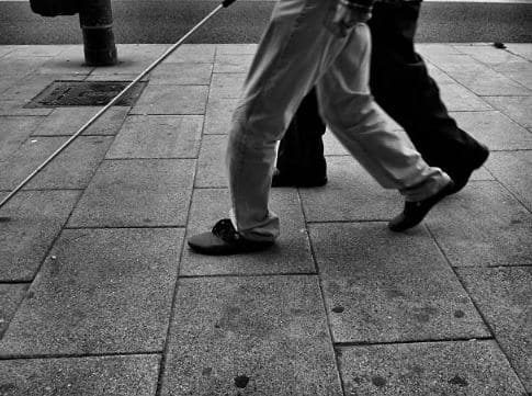 Personne malvoyante qui marche sur un trottoir avec une canne d'aveugle